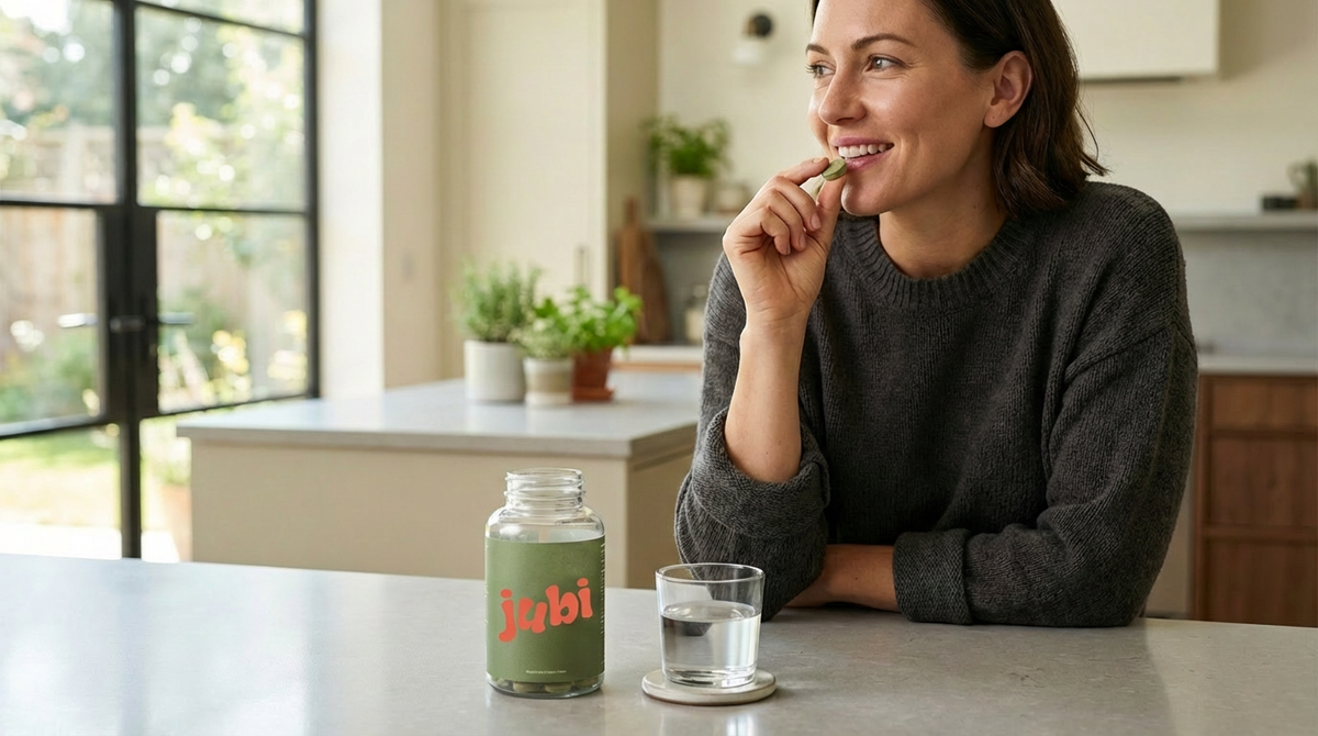 Customer in a bright kitchen holding a chewable tablet with Jubi 7OH Chewables bottle on the counter